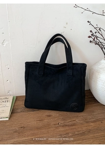 Close-up of black minimalist tote bag with circular embossed logo on a wooden table