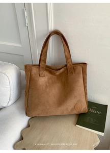 Detail of a brown suede tote bag with minimalist logo on a modern white surface