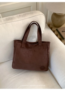 Detail of coffee brown suede tote bag with leather logo on a sofa in retro setting