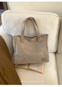 Detail of minimalist sand beige tote bag with circular logo emblem on soft white sofa