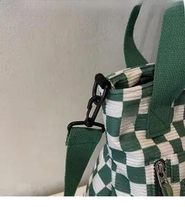Close-up of green checkered corduroy tote bag showing metal zipper and durable strap hook