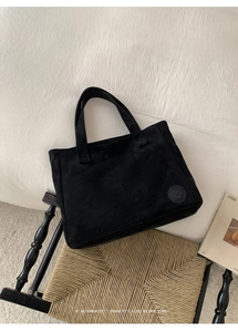 Detail of minimalist black faux suede tote bag with circular embossed logo and texture