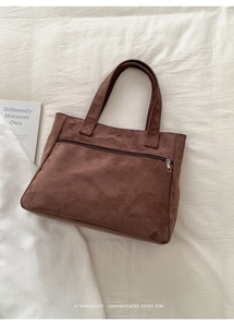 Detail of dark brown suede tote bag with front zipper pocket and reinforced stitching