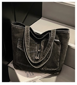 Detail of a large denim tote bag featuring utility pockets and washed black fabric