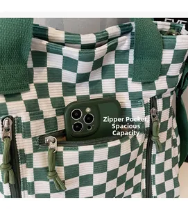 Close-up of green checkered corduroy tote bag showing front zipper pocket with smartphone