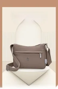 Detail view of taupe waterproof nylon shoulder bag featuring HAO YUN logo on a white pedestal