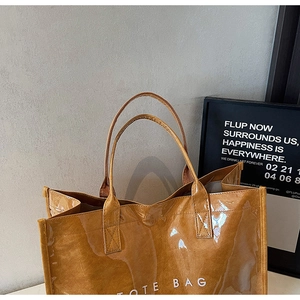 Detail view of brown glossy tote bag with white TOTE BAG text and stylish shoulder straps
