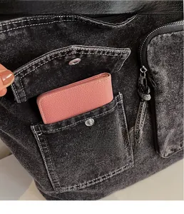 Detail of a black denim tote bag with front pocket showing white contrast stitching