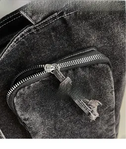 Detailed close-up of a smooth metal zipper on black washed denim tote bag with frayed edges