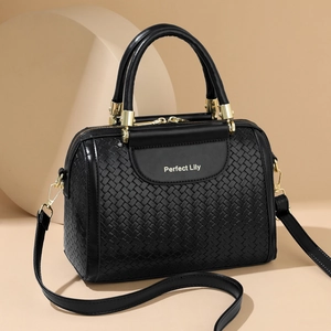 Elegant black woven Boston bag with dual handles and gold hardware in minimalist studio set