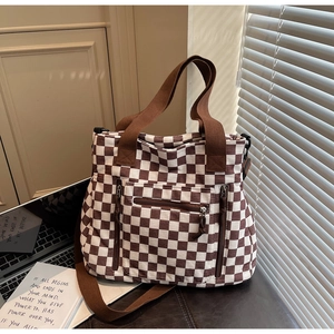 Close-up of checkerboard tote bag with multiple zipper pockets on a textured surface