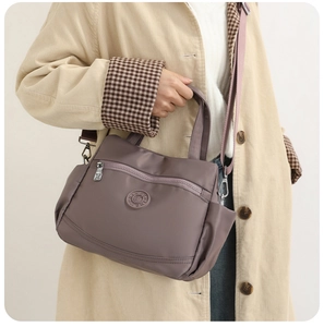 Detail of purple nylon handbag with metal zipper and adjustable shoulder strap worn by model
