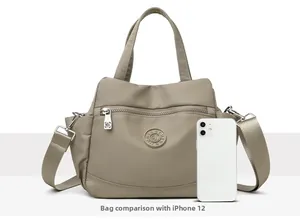 Size comparison between the beige nylon crossbody bag and an iPhone 12 for scale