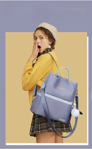 Dettaglio dello zaino in nylon viola con cinghie blu a contrasto e pompon bianco