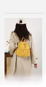 Detail view of yellow nylon backpack with pleated texture worn over a beige coat