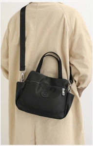 Side view of a large black nylon multi-layer shoulder bag worn with a corduroy coat