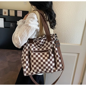 Detail of checkered canvas tote bag featuring functional front zippers and adjustable straps