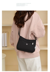 Side view of black nylon crossbody bag worn by a model in a cozy indoor setting