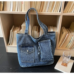 Detail of blue washed denim tote bag showing functional exterior pockets and washed texture