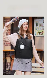 Outdoor shot of a black waterproof oxford backpack featuring a plush white ball charm