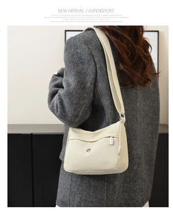 Detail of cream nylon crossbody bag showing zip pockets and adjustable strap on a model