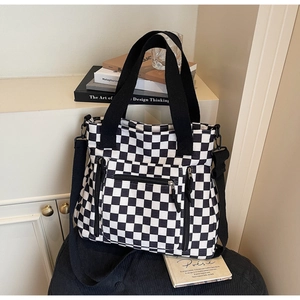 Detail of checkered tote bag with zipper pockets and adjustable black strap on a desk