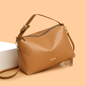 Brown woven texture tote bag with gold hardware and shoulder strap in a minimalist setting