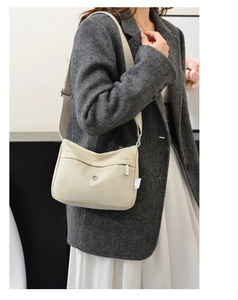 Detail view of adjustable wide shoulder strap and brand tag on beige nylon crossbody bag