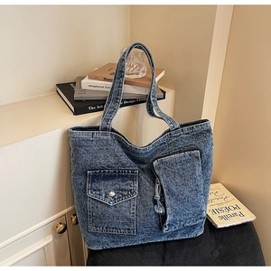 Detail of blue denim tote bag featuring utility pockets and washed texture on a desk