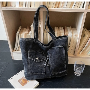 Close-up of distressed denim tote bag featuring dual pockets and metallic hardware detail