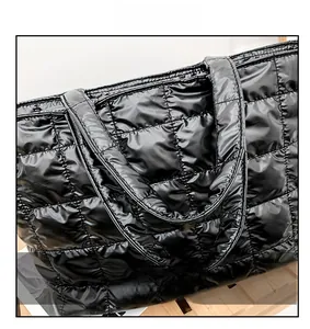Detail of soft padded handles on black quilted tote bag with shiny finish