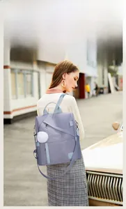 Outdoor street style view of a casual lavender oxford fabric backpack with a white plush pompom