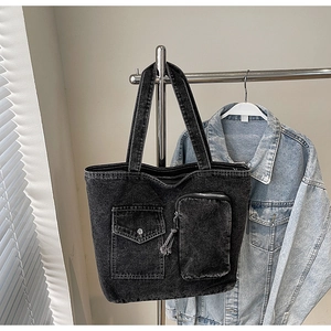 Detail of black washed denim tote bag featuring front flap pocket and white stitching