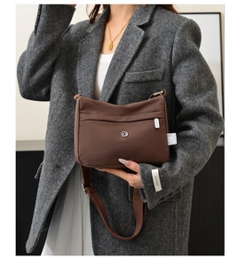 Brown nylon crossbody bag shown on a model wearing a grey coat and a white dress