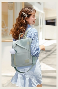 Side view of woman wearing a mint green oxford fabric backpack with white pompom detail