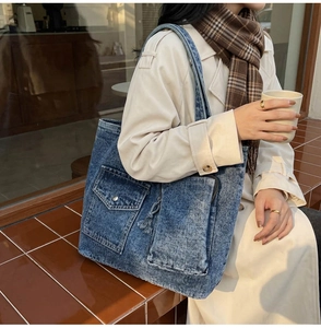 Detail of blue denim tote bag featuring front flap pocket and sturdy wide shoulder strap