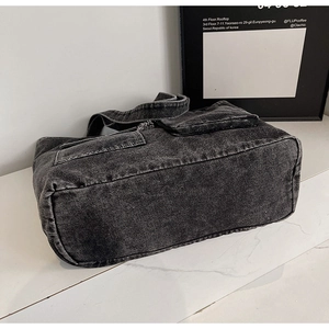 Detail view of the rectangular bottom and flap pocket on a washed denim tote bag
