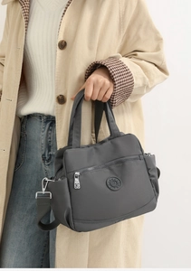 Close-up of grey nylon crossbody bag showing the round logo and multi-pocket design