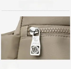 Detail of silver metal zipper with engraved logo on khaki nylon multi-layer handbag
