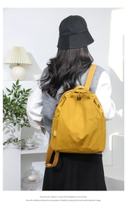 Ginger yellow waterproof nylon backpack shown on model in a cozy interior setting