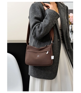 Detail of dark brown nylon crossbody bag with wide woven strap on a model wearing a suit