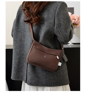 Detail of dark brown nylon crossbody bag with hidden zipper and white side label