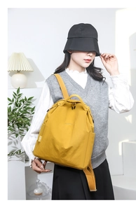 Detail view of mustard yellow water-resistant nylon backpack on model in home setting