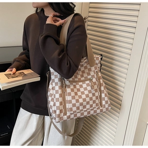 Detail of checkered tote bag showing functional front zipper pockets and wide fabric straps