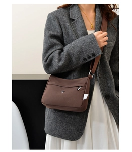 Detail of a brown nylon crossbody bag with metallic logo and smooth zipper on a blazer