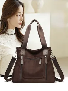Detail of dark brown suede tote bag featuring three front zip pockets and wide strap