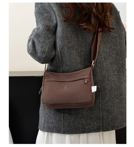 Detail view of water-resistant nylon shoulder bag with adjustable strap on a grey blazer