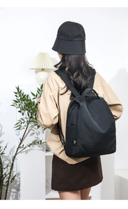 Side detail of a black nylon backpack with a woven brand logo label and zipper closure