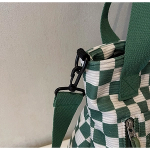 Detail of green checkerboard corduroy tote bag showing metal zipper and strap hook