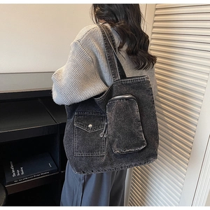 Close-up of washed black denim tote bag showing detailed utility pockets and metallic zippers